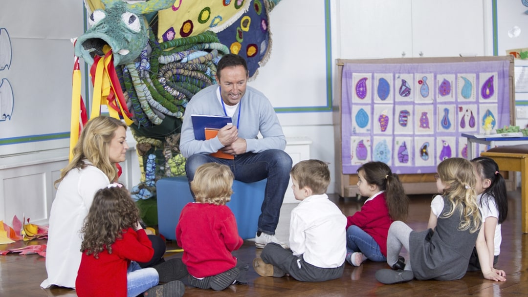 Male teacher reading to group of children in hall