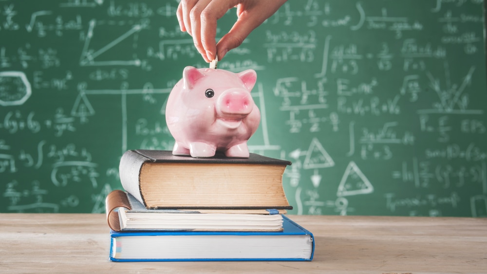 buy more save more- teacher putting coin into piggy bank on desk